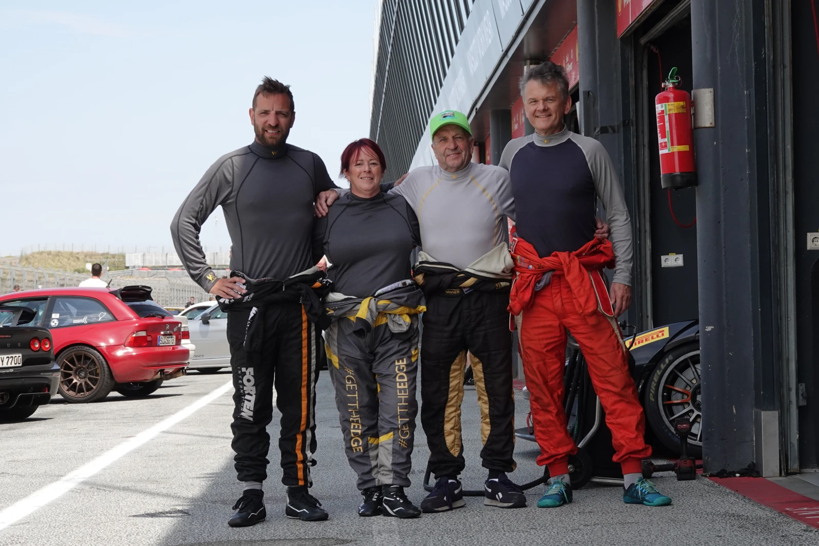 Four drivers in Walero base layers, race suits half-peeled, in the pit lane
